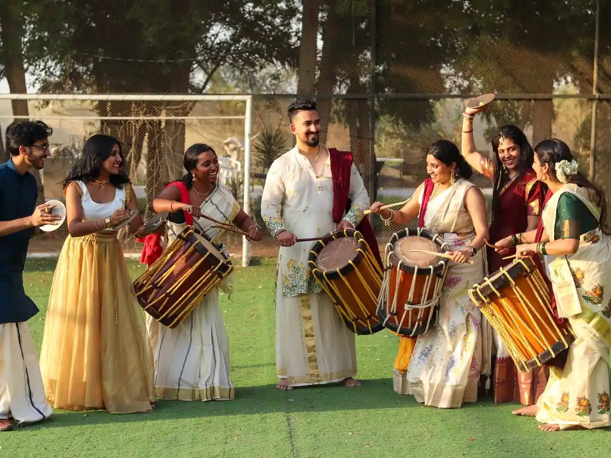 Traditional Kerala Chendamelam troupe performing with energetic drumbeats, wearing traditional white mundu attire under warm outdoor event lighting.