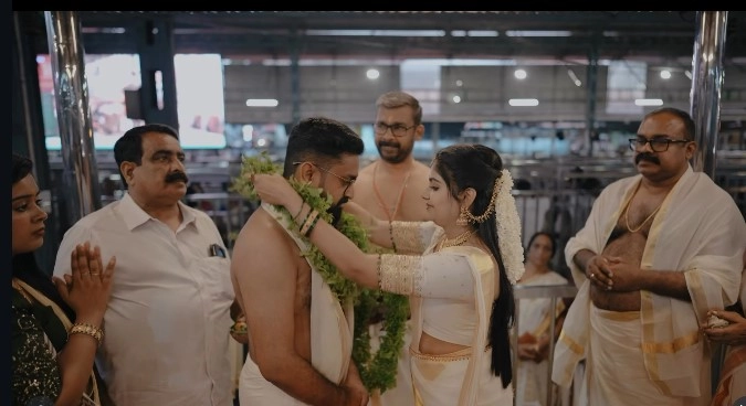 Bride and groom exchanging traditional fresh Thulasi and floral garlands on the kalyana mandapam stage during their Guruvayur Temple wedding ceremony.