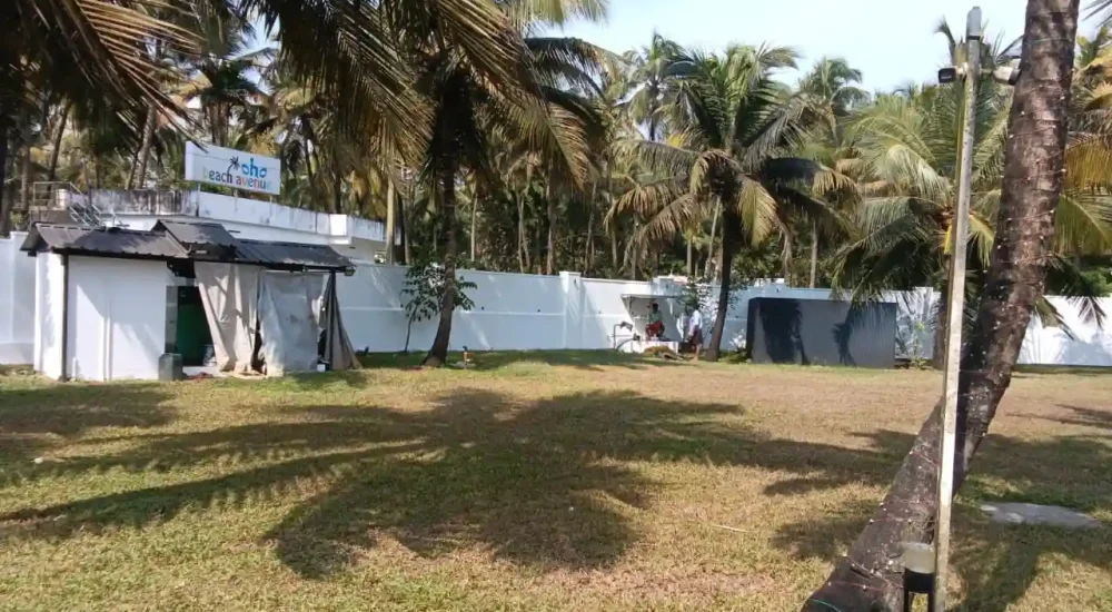 Outdoor lawn setup at Deja Blu showing a white compound wall, coconut palms, and the OHO Beach Avenue sign.
