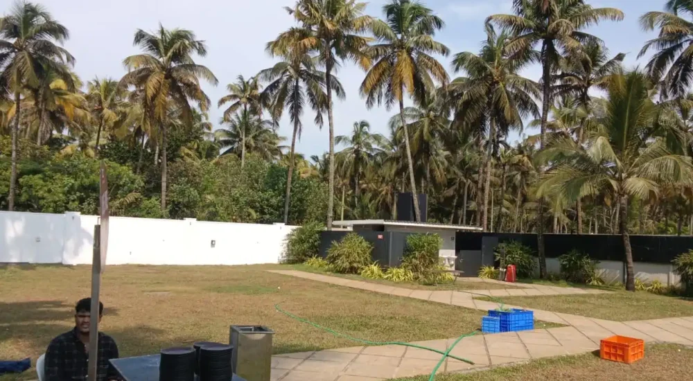 Outdoor event preparation at Deja Blu with staff member seated at a service table, paved walkways, and coconut palms.
