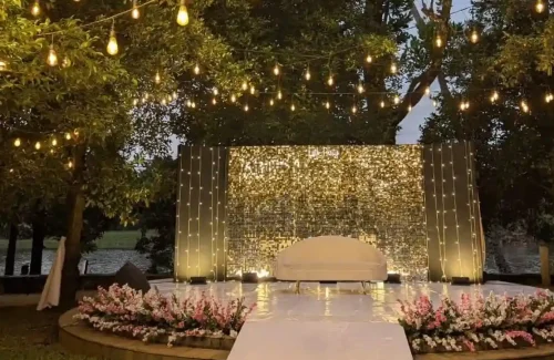 Elegant daytime wedding mandap design at riverine farm villa in kochi featuring a clean wooden archway adorned with cascading white wisteria flowers. by Melodia event management