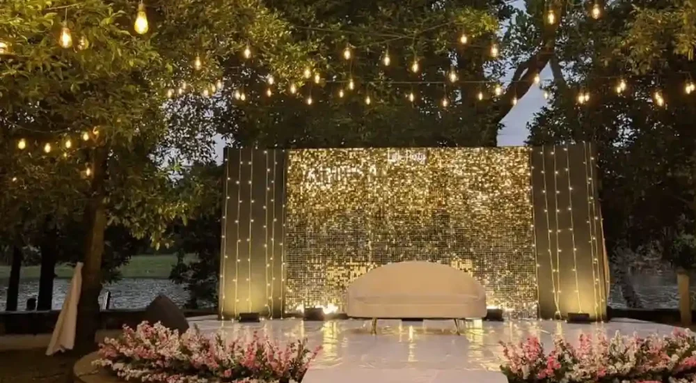 Elegant daytime wedding mandap design at riverine farm villa in kochi featuring a clean wooden archway adorned with cascading white wisteria flowers. by Melodia event management