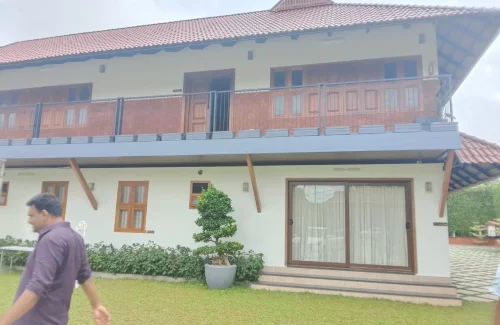 Arcadia Resort & Banquet ,Traditional Kerala-style villa with wooden pillars and porch, overlooking a spacious paved courtyard with diamond grass lattice and a tall green vine wall.