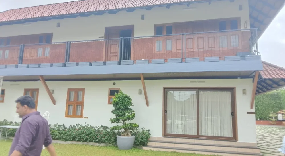 Arcadia Resort & Banquet ,Traditional Kerala-style villa with wooden pillars and porch, overlooking a spacious paved courtyard with diamond grass lattice and a tall green vine wall.