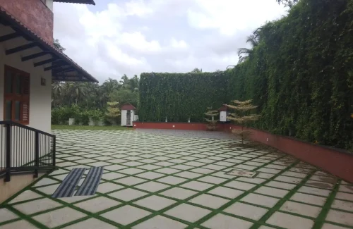 Arcadia Resort & Banquet ,Diamond paver courtyard leading toward a central green lawn, flanked by a dark wooden cottage and a pitched red-tile roof dining pavilion.