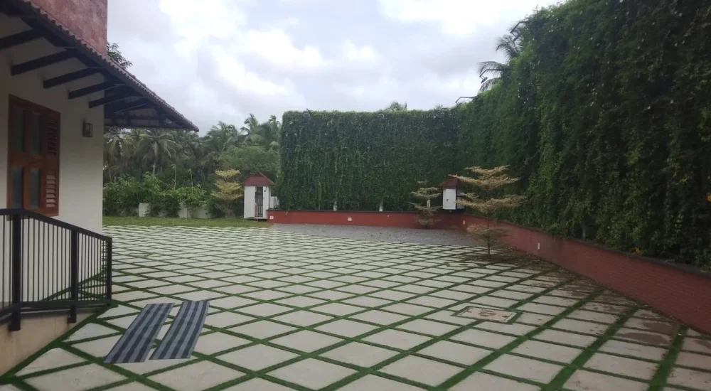 Arcadia Resort & Banquet ,Diamond paver courtyard leading toward a central green lawn, flanked by a dark wooden cottage and a pitched red-tile roof dining pavilion.