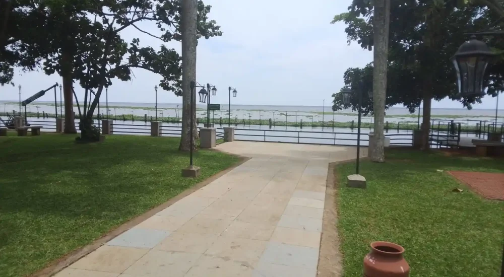 Expansive waterfront lawn and paved pathway leading to the open-air event stage overlooking Vembanad Lake at Backwater Ripples Hotel Kumarakom.