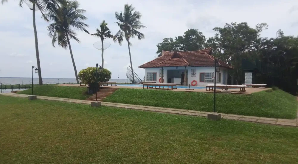 Poolside event lawn and outdoor reception space with traditional cottage architecture and palm trees at Backwater Ripples Hotel Kumarakom.