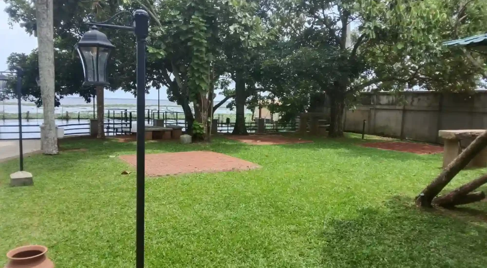 Scenic garden lawn area with stone paving and vintage lampposts overlooking the water at Backwater Ripples Hotel Kumarakom.