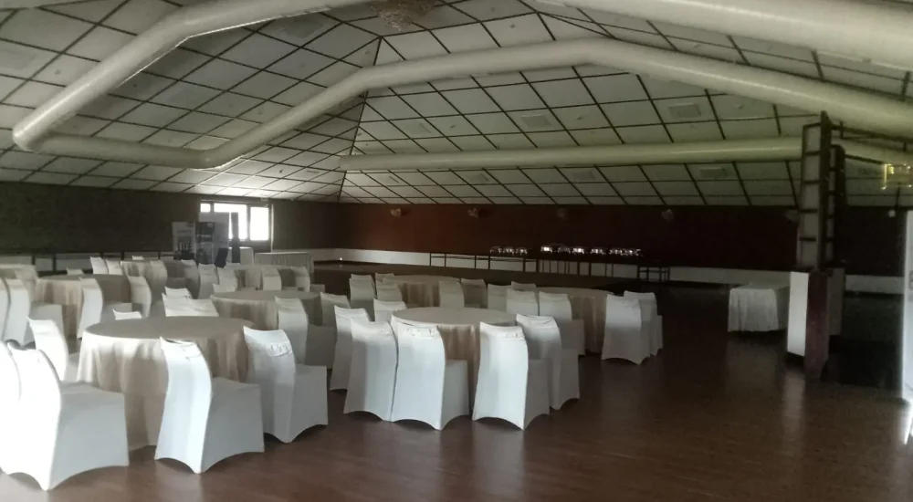Spacious indoor Central Court banquet hall set up with round dining tables and white-covered chairs for weddings and corporate events at Backwater Ripples Hotel Kumarakom.