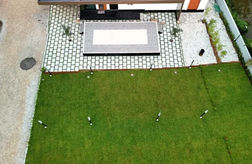 Top angle drone view showing the outdoor lawn, built-in stage, and paved walkway at Coconut Groves Kanjiramattom.
