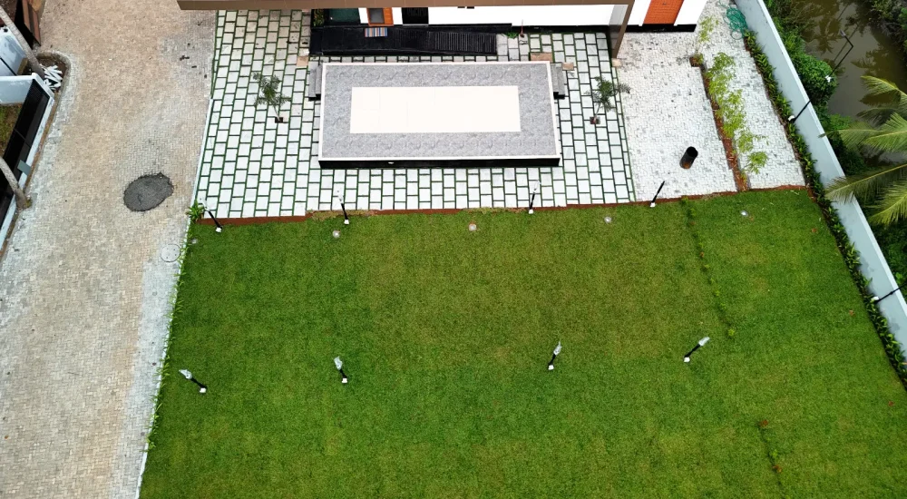 Top angle drone view showing the outdoor lawn, built-in stage, and paved walkway at Coconut Groves Kanjiramattom.