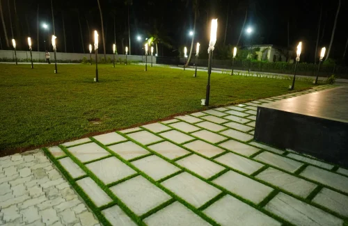 Night view of the open lawn with paved walkway and glowing garden light poles at Coconut Groves venue.