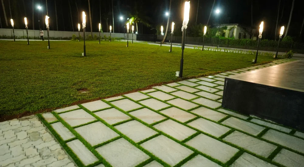 Night view of the open lawn with paved walkway and glowing garden light poles at Coconut Groves venue.