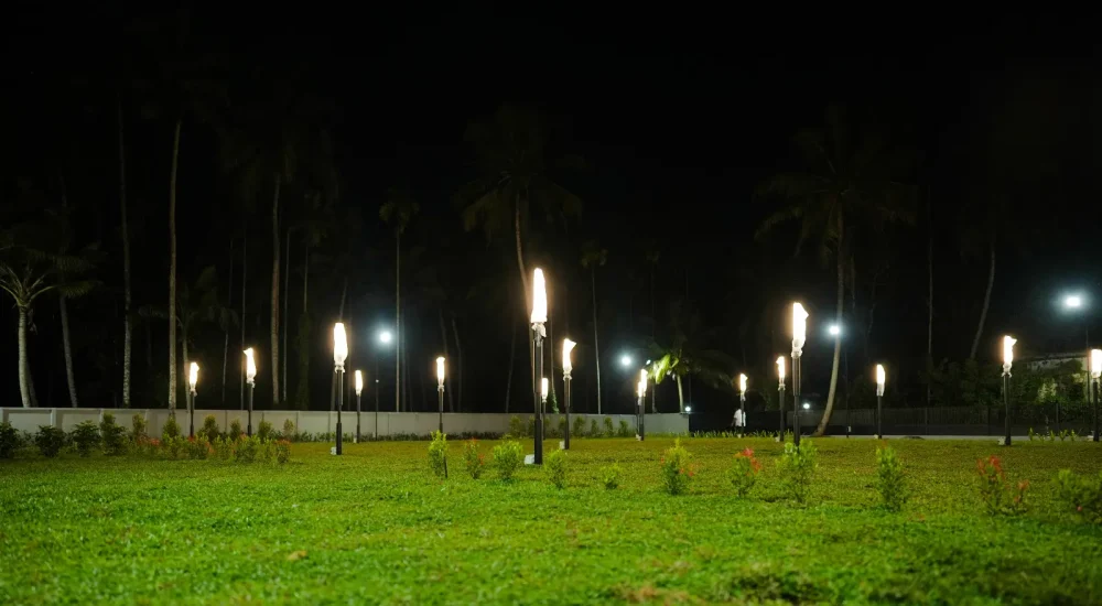 Illuminated open-air wedding lawn with garden pole lights at night at Coconut Groves Kanjiramattom.