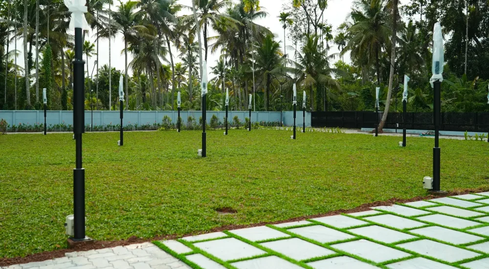 Daytime view of the green open-air reception lawn surrounded by coconut palms at Coconut Groves Kanjiramattom.