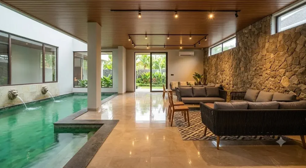 Premium indoor poolside lounge area at Devi Event Resort Thrissur, featuring a sleek swimming pool with lion fountains, modern seating, and an elegant stone accent wall.