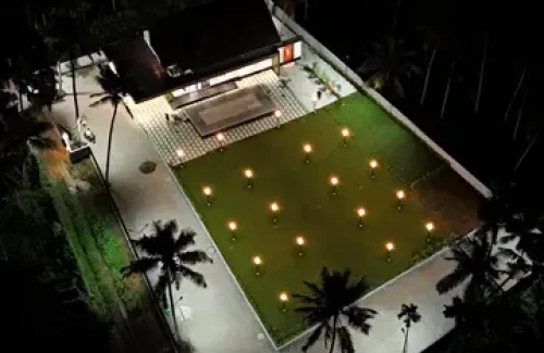 Top angle drone view showing the outdoor lawn, built-in stage, and paved walkway at Coconut Groves Kanjiramattom.