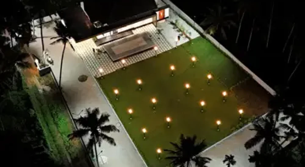Top angle drone view showing the outdoor lawn, built-in stage, and paved walkway at Coconut Groves Kanjiramattom.