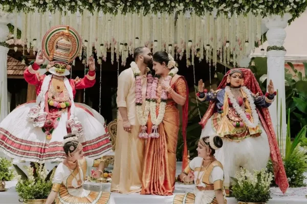 A vibrant indoor traditional Kerala wedding ceremony at Guruvayur with around 300 seated guests watching the bride and groom exchange garlands on a floral-decorated stage.