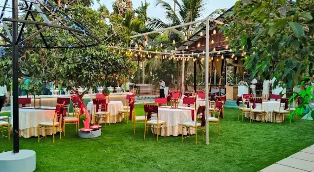 Night view of the open green lawn at Mankara Farms, featuring guest round-table seating setups with gold-bow chairs arranged under a magnificent warm-toned fairy light canopy designed by Melodia Event Management