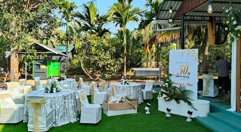 Daytime view of the open lawn at Mankara Farms in Puthenchira, showcasing a spacious guest seating arrangement with elegant round tables, premium linen tablecloths, and decorated chairs meticulously laid out by Melodia Event Management.