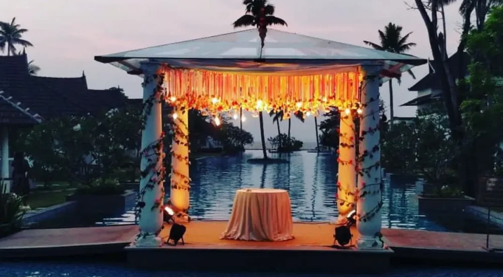 Illuminated floating mandap setup with warm string lights over swimming pool at Rhythm Kumarakom resort