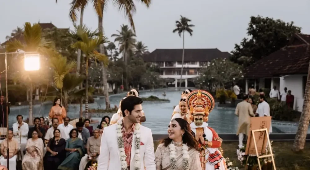 Bride and groom walking down floral white carpet walkway with Kathakali artist performance at Rhythm Kumarakom outdoor lawn