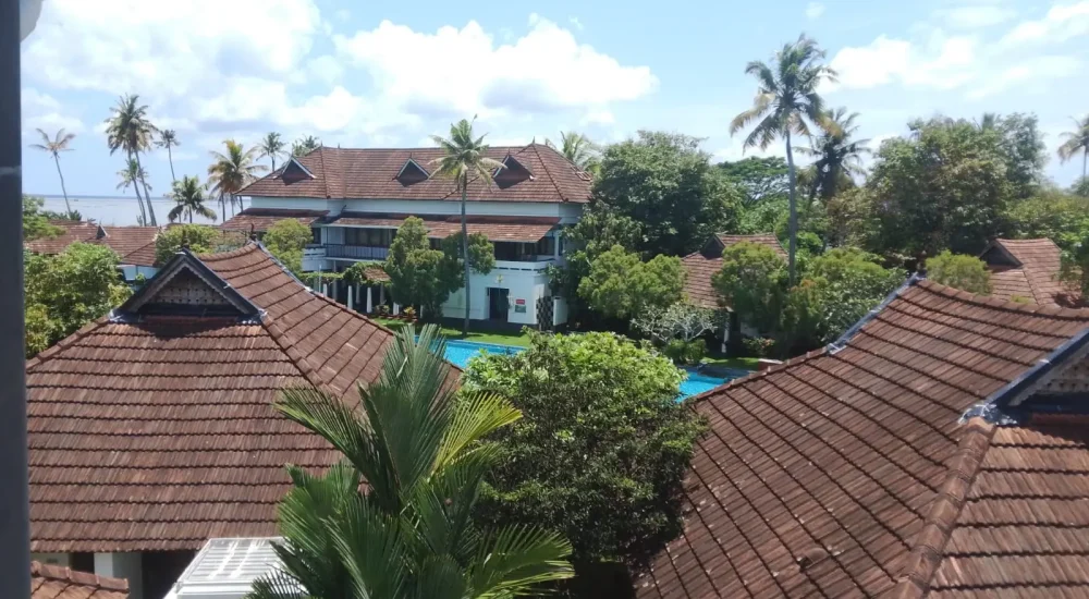 Aerial view of traditional Kerala style tiled roofs and swimming pool surrounded by greenery at Rhythm Kumarakom